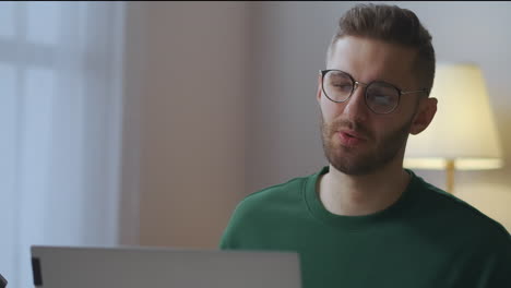 young-male-specialist-is-discussing-working-questions-with-colleagues-during-online-meeting-speaking-to-web-camera-of-laptop-portrait-in-home-office